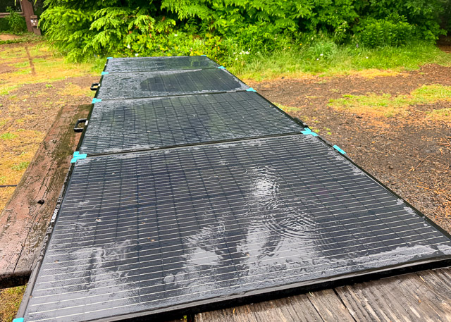 Rain falling steadily on solar panels that are resting on a picnic table.